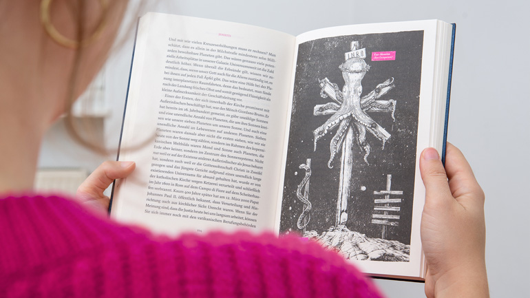 Fotografie einer Person die eine großflächige Illustration im Buch betrachtet.