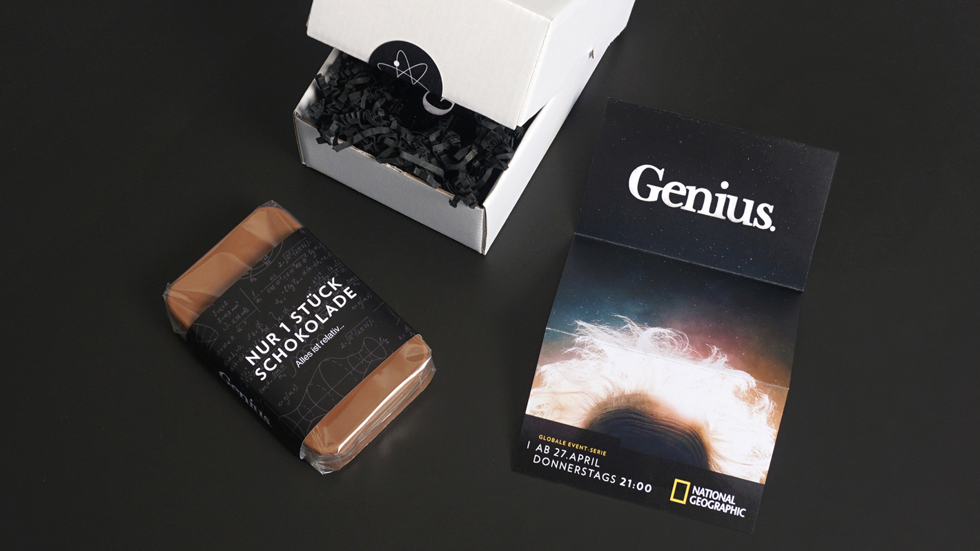 Fotografie der Einzelteile der Box. Die Schokolade, ein Flyer mit Auflösung und die weiße Verpackung.