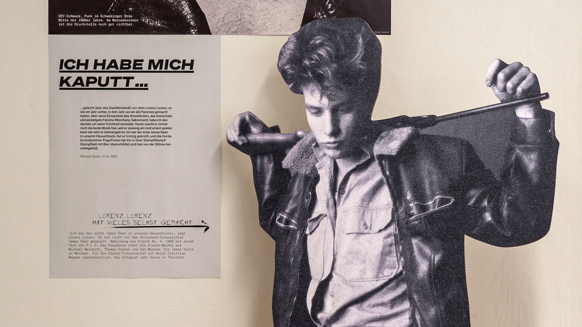 Details der Ausstellung vor beiger Wand. Schwarz-weißer Aufsteller eines jungen Mannes mit Gewehr und ein graues Plakat mit der Headline: „Ich habe mich kaputt…“.