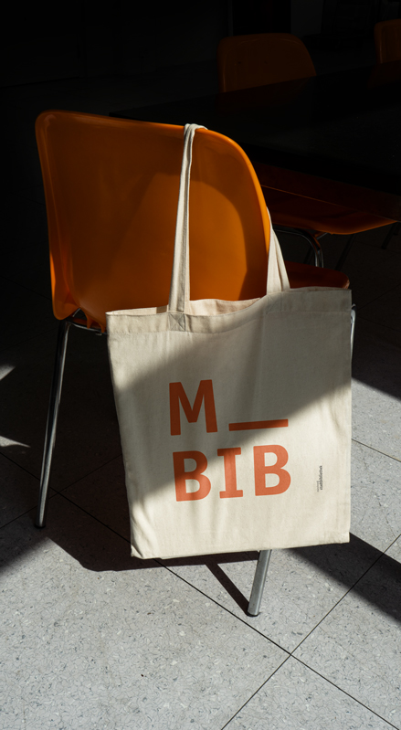 Ein Jutebeutel mit M_BIB Aufdruck hängt über einen Bibliotheksstuhl.
