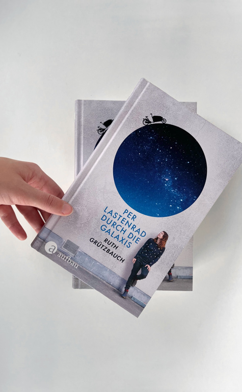 Fotografie des Buchcovers. Auf dem Cover sind eine Frau und ein Kreis. Durch den Kreis kann man eine Galaxie sehen.