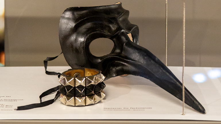 Schwarze Maske mit Schnabel und Armband mit Nieten.