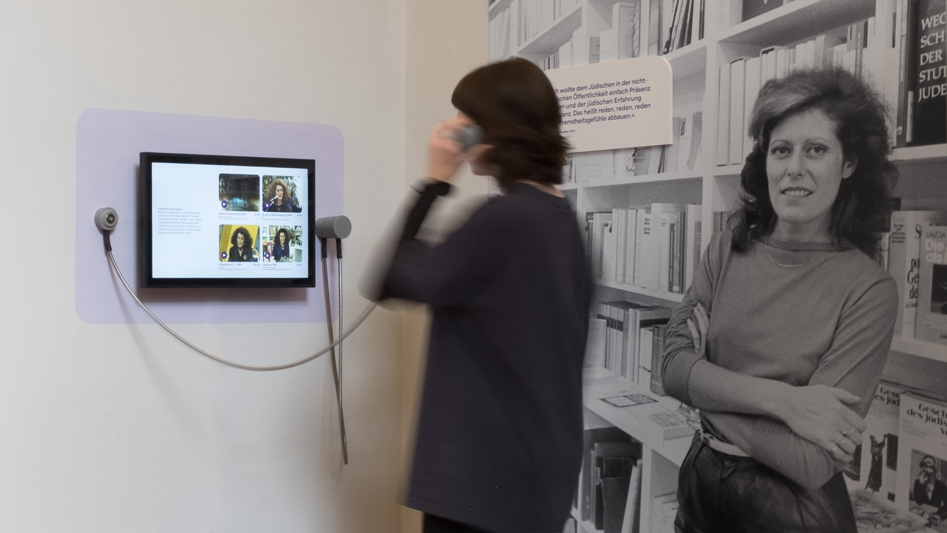 Interaktive Hörstation mit Porträtaufnahmen vor Bücherregal, Teil der Ausstellungsgestaltung