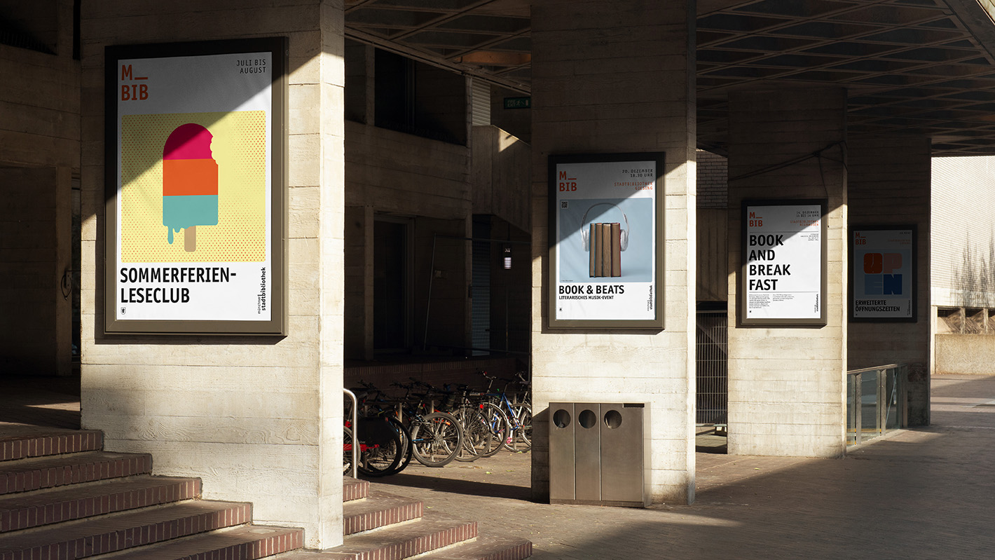 Eingangsbereich einer Bibliothek, in dem 4 verschiedene M_BIB-Plakate an verschiedenen Säulen aufgehängt sind.